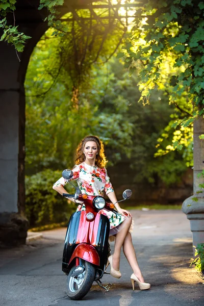 Beautiful middle-aged woman with curly hair sits on a scooter in a dress. — Stock Photo, Image