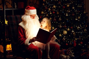 Noel Baba ve mutlu küçük bir kız sihirli bir kitap izliyor Noel Baba 'nın kucağında oturan bir çocuk