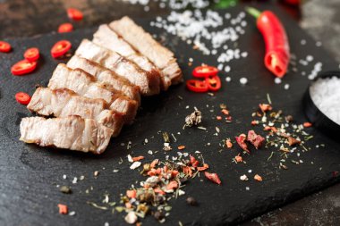 Tavada pişirilmiş domuz eti ve arka planda bulunan baharatlarla dilimlenmiş.