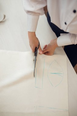 Kapatın. Kadın terzi, terziden aldığı tebeşirle yaptığı elbisenin kalıbını belirlemek için bir rulo kumaş kesiyor..