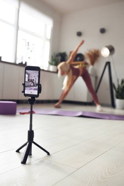 Genç, güzel sarışın karantina sırasında vücuduna bakıyor. İnsanları internetten cep telefonuyla eğitiyor..