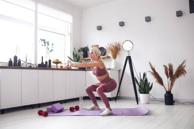 Genç, güzel sarışın karantina sırasında vücuduna bakıyor. İnsanları internetten cep telefonuyla eğitiyor..