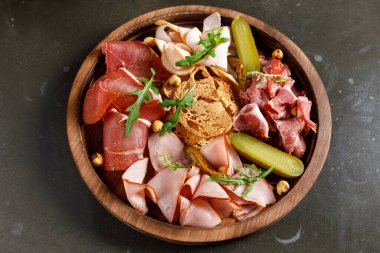 Prosciutto, salam, peynir, ekmek çubukları ve koyu taşlı arka planda zeytinlerle kesme tahtası. Yukarıdan bakıldığında