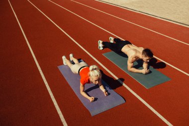 Stadyumda spor yapan genç çift yoga minderlerinde yatıyor.