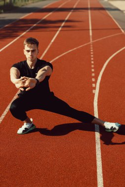 Okul stadyumunda spor öncesi ısınma egzersizi yapan genç adam.