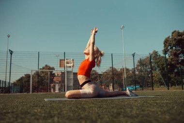 Güzel sarışın bir futbol sahasının çimlerinde geriniyor.
