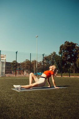 Güzel sarışın bir futbol sahasının çimlerinde geriniyor.