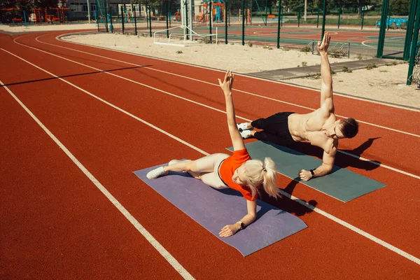 一对年轻夫妇躺在瑜伽垫上在体育馆里做运动 — 图库照片