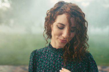 Şirin kızıl saçlı kıvırcık kız şehir merkezindeki sislerin altında seviniyor.