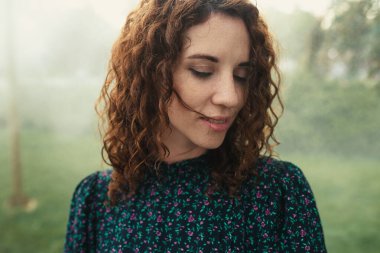 Şirin kızıl saçlı kıvırcık kız şehir merkezindeki sislerin altında seviniyor.