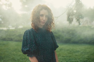 Şirin kızıl saçlı kıvırcık kız şehir merkezindeki sislerin altında seviniyor.