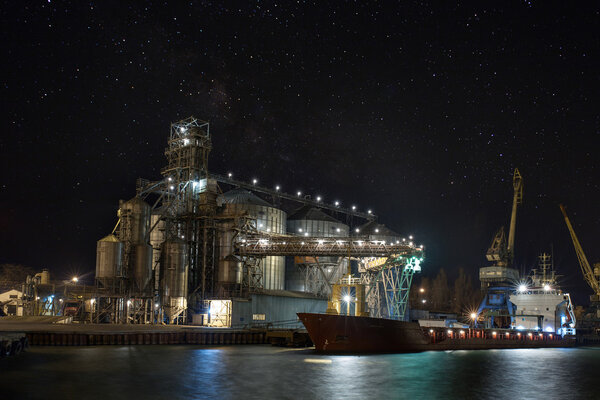 Cargo crane, ship and grain dryer in port. At night