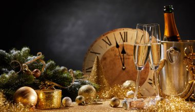Wide angle New Years banner with flutes and a bottle of champagne in front of a clock counting down to midnight and copy space above assorted gold seasonal holiday decorations clipart