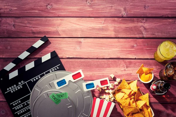 Various movie and film props including a clapperboard alongside popcorn, 3d glasses, tickets and refreshments in a cinematography themed image with timber wood grain copy space.