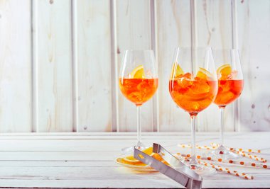Refreshing aperol spritz cocktails with straws and sliced orange on a white timber table. clipart
