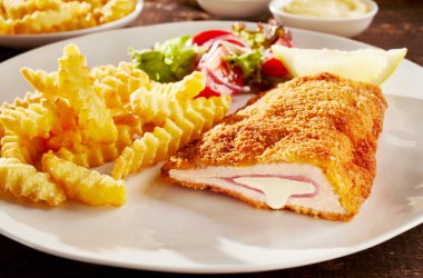 Piece of fried cordon bleu chicken served with french fries and salad on plate clipart