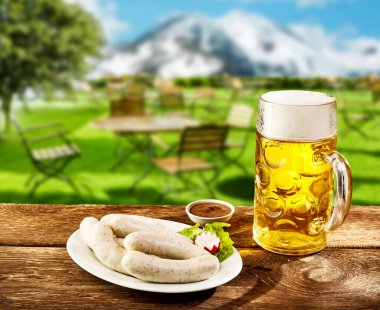 Traditional Oktoberfest cuisine with a plates of weissworst or veal sausages with a savory dip on a rustic tavern table with a glass of lager in the Bavarian Alps clipart