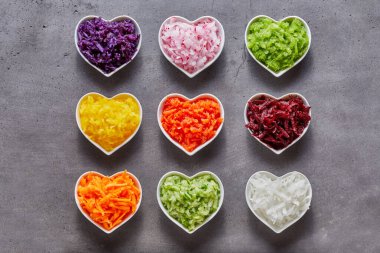 Heart-shaped bowls with healthy grated vegetable ingredients of different colors shot from above on grey background clipart