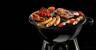 Variety of different meat grilling on a portable barbecue over a dark background with copy space in panoramic banner or header format clipart