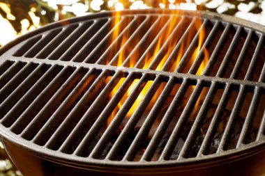 Flaming coals in a portable summer barbecue with the empty grill on top outdoors in the garden with sparkling sunlight bokeh clipart