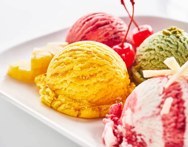 Variety of creamy Italian ice cream or gelato served in scoops on a single plate with fresh fruit ingredients to the side with focus to colorful yellow pineapple ice-cream