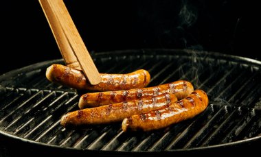 Four sausages cooking on a portable barbecue grilling over the hot coals with a dark background with copy space clipart