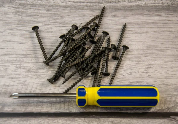 Black self-tapping screws and a curly screwdriver. — Stock Photo, Image