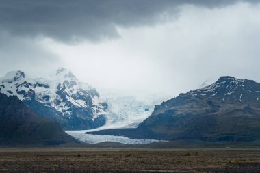 Buzul İzlanda 'da çok bulutlu ve yağmurlu bir günde dağdan aşağı kayar. Vahşi kutup manzarası. Kara bulutlar buzulun üzerinde toplanıyor..