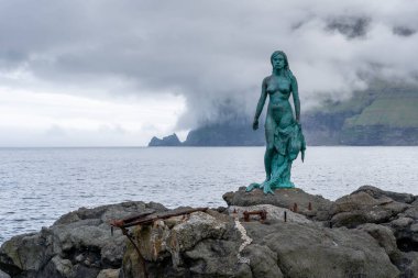 Mikladalur, Faroe Adaları - 06.12.2017: Fok Kadın Heykeli Mikladalur, Kalsoy 'un kayalık kıyılarında, arkasında okyanus anc dramatik bulutlarla. Vahşi Faroe Adaları 'nda sabah geç saatlerde.