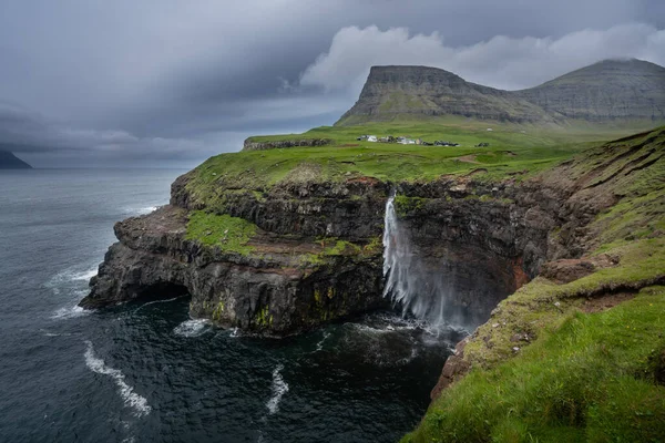 Meşhur Mulafossur şelalesinin uçurumdan güçlü kanatlarla okyanusa düştüğü haberi. Faroe Adaları 'nda bulutlu, rüzgarlı bir hava var. Gasadalur köyü arkada..