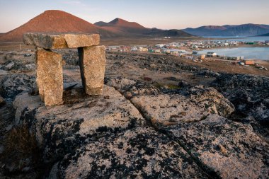 Çıplak tepeler ve okyanuslarla dolu sert bir kuzey kutbu manzarasında alacakaranlık. Arka planda Eskimo yerleşimi olan Inuksuk Qikiqtarjuaq. Broughton Adası, Nunavut. Kuzey..