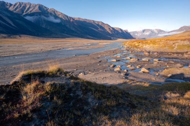 Kuzey Kutbu uzak vadisindeki Baykuş Nehri yatağı, Akshayuk Geçidi, Nunavut. Güneşli bir öğleden sonra, güzel kutup manzarası. Uzak ufuktaki ikonik dağlar. Sonbahar renkleri. Vahşi kuzey.