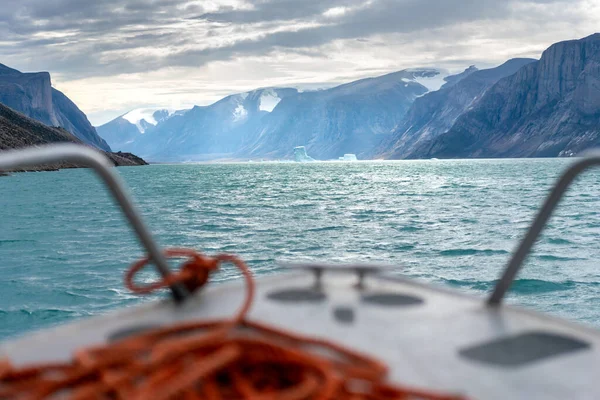 デイビス海峡の水の中に浮かぶ険しい崖や氷山と北パンニールトゥングフィヨルド 小さな船から見た北極の荒野 劇的な光だ — ストック写真