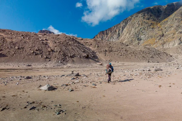 Bulutlu bir günde, uzak kutup vadisinde ağır bir sırt çantasıyla yürüyen bir yürüyüşçü. Kanada, Baffin Adası, Akshayuk Geçidi 'nin dramatik arktik manzarası. Önünde kum tepeciği var..