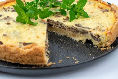 Yakın çekim geniş stüdyo resmi taze pişmiş sarı Fransız tuzlu keki, veya kiş, mantarlı ve yeşil naneli, siyah bir tasarım tabağında, beyaz arka planda izole edilmiş.