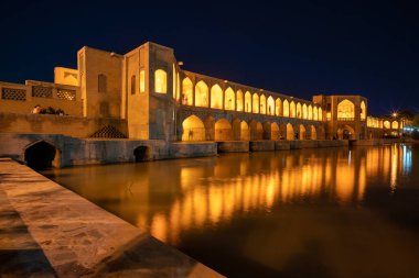 14.04.2019 - İsfahan, İran: İran 'ın İsfahan kentindeki ünlü Khajoo Köprüsü. Sarı ve turuncu ışıklarla aydınlatılmış eski taş köprü suya yansıyor.