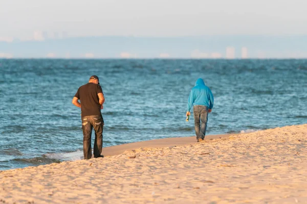 Dos hombres caminando en una playa junto al mar Báltico lejos del espectador en la madrugada del verano, con la orilla en la neblina en el horizonte distante. Después de la fiesta. — Foto de Stock