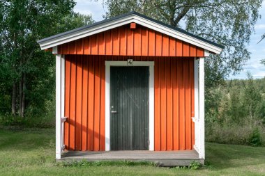 Anaset, İsveç - 08.22.2021: Beyaz pencere ve kapı çerçeveli tipik kırmızı ahşap İsveç kulübesinin dışı. İsveç 'te kamp yapmak. Yaz tatili ve İskandinavya 'da seyahat.