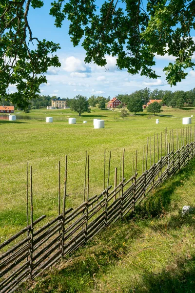 Vertical shot of a small settlement farm in sourthern Sweden on a beautiful sunny summer day. Holiday in Swedish countryside. Vintage fence and white heystacks. — Stock Photo, Image