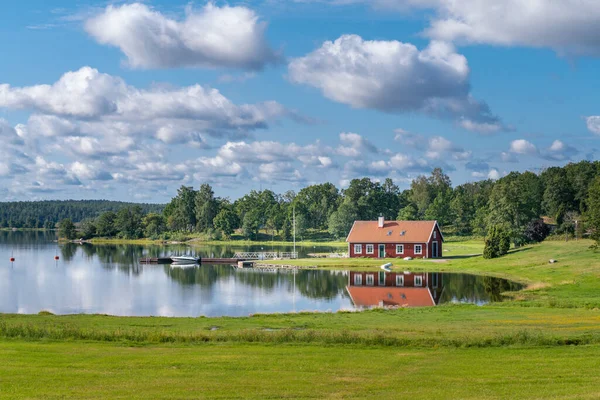 Typical red wooden house in countryside by the sea in natire of southern Sweden on a beautiful sunny summer day. Relaxing rural landscape. Reflection on water surface. Holiday in Sweden. — Stock Photo, Image