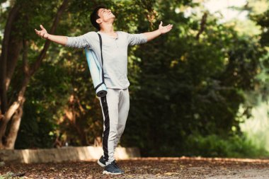 Latin genç adam nefes almak için kollarını açıyor ve ormanda yürüyor.