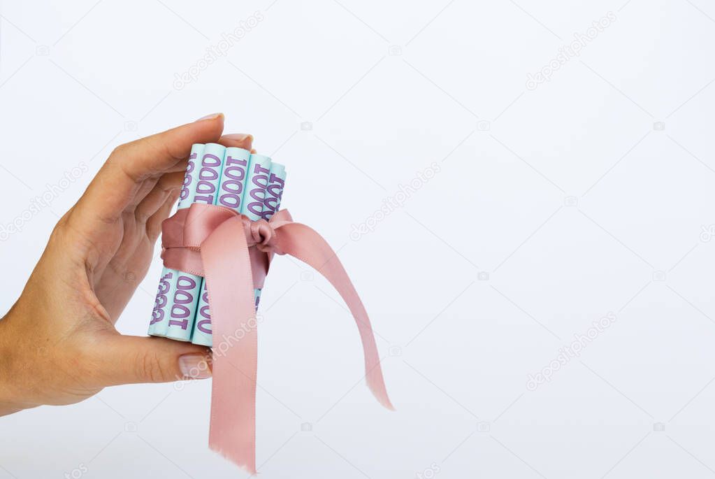 Ukrainian money wrapped with a gift ribbon in a hand.