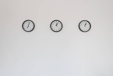 Açık gri duvar arka planında üç klasik saat asılı..