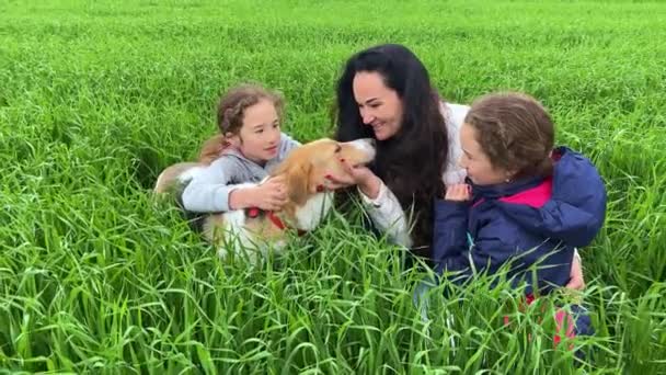 4К Мать с дочерьми и их собака сидят на траве. — стоковое видео