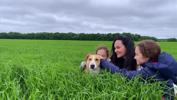 4k Fröhliche Mutter mit ihren Töchtern und ihrem Hund auf der grünen Wiese. — Stockvideo