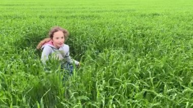 4k sevimli küçük kız yeşil çimenlerde oturuyor, gülümsüyor ve etrafa bakıyor..