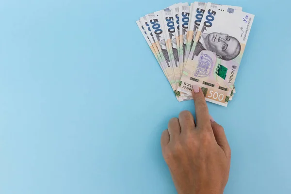 Puntos de dedo en el dinero. Grivna ucraniana. Sobre un fondo azul. — Foto de Stock