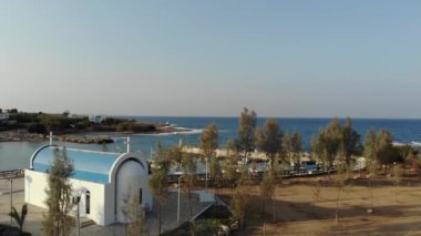 4k Havadan Yunan tarzı bir kilise, tekneli iskele ve mavi deniz manzarası. 