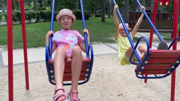 4k Irmãs gêmeas alegres balançando em um balanço em um playground. — Vídeo de Stock