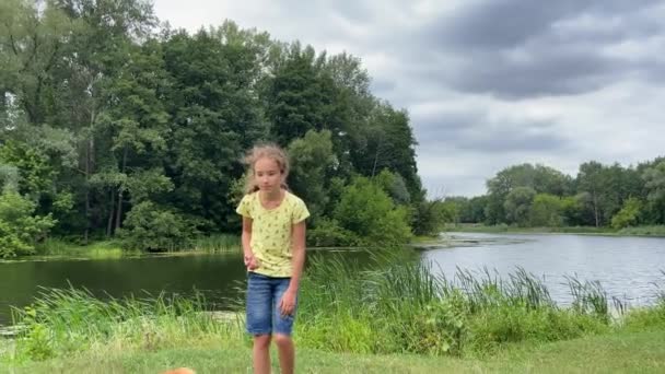 4k Kleines Mädchen trainiert den Hund auf der Wiese am Fluss. — Stockvideo